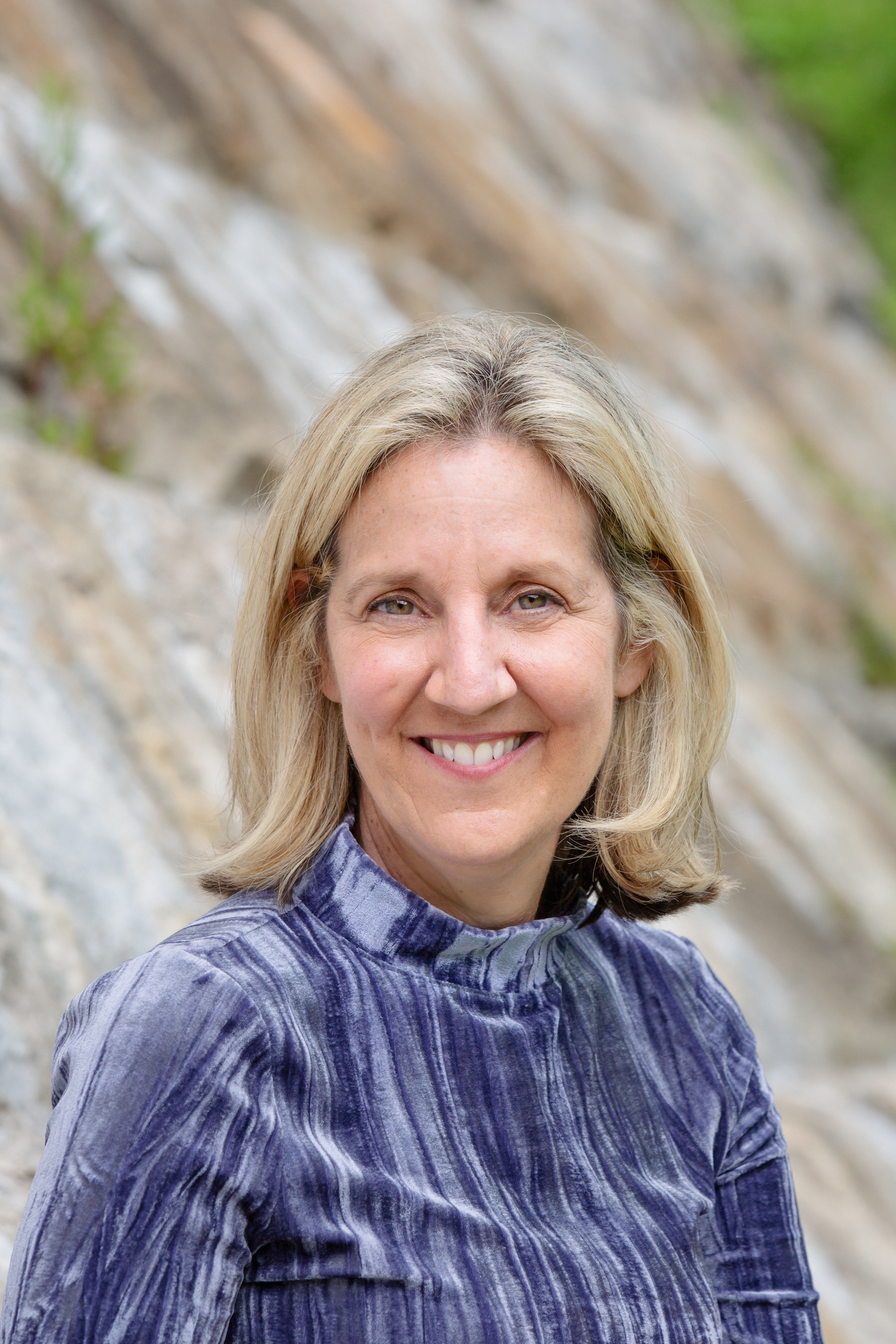 a woman with shoulder-length blonde hair and a blue shirt smiles at the camera.