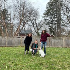 Three people standing with dog in yard.