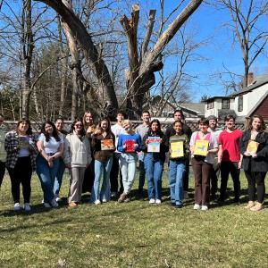 Photo of students holding books and standing outside.