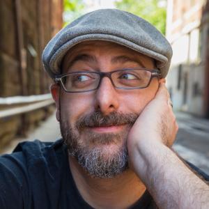 Photo of author wearing hat, with hand on cheek.