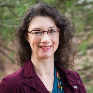 Photo of author with long dark hair, glasses, and purple jacket.