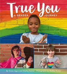 Three children stand smiling against a brick wall painted rainbow colors.