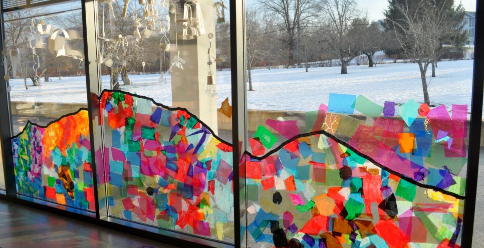 A colorful tissue-paper-collage mountain across three panels of windows.