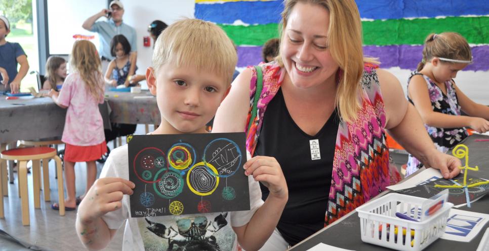 An adult and child smiling and holding up their circle-stamped paper.