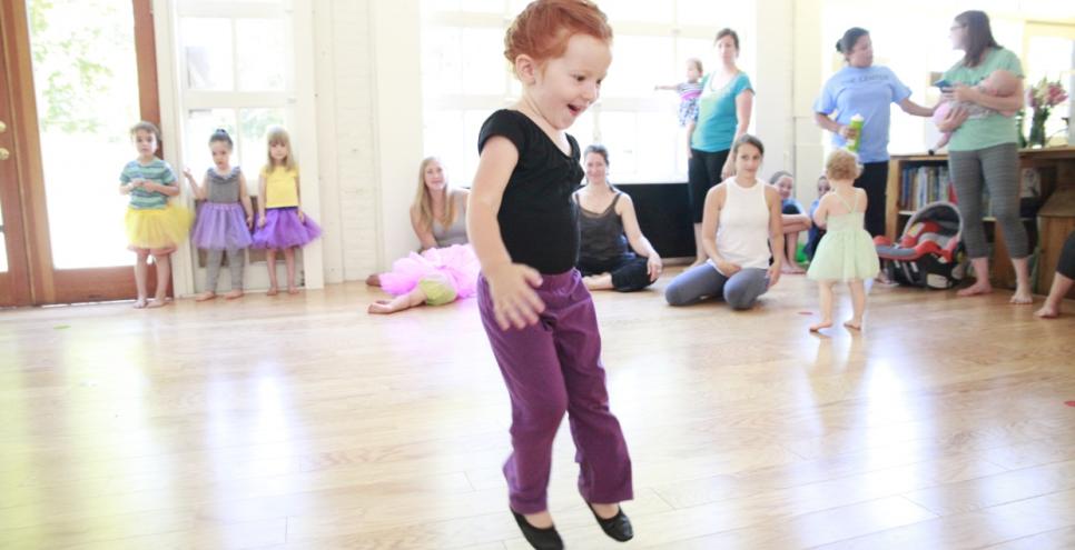 A young child jumps in the air as families watch in the background.