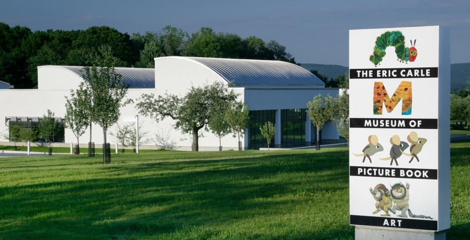 The Eric Carle Museum building with the Eric Carle Museum sign in front of it, surrounded by green grass. 