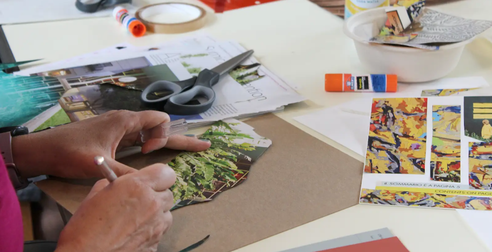 Close up of hands working with collage materials, papers, pencils, tape, and glue.