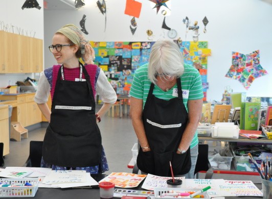 Two participants smiling and looking at other people's artwork