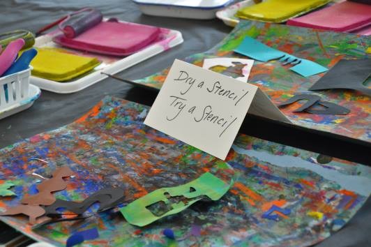 Sign reading "dry a stencil, try a stencil" standing on a paint covered drying mat. 