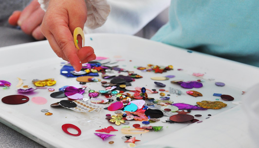 toddler sticking sequins to contact paper