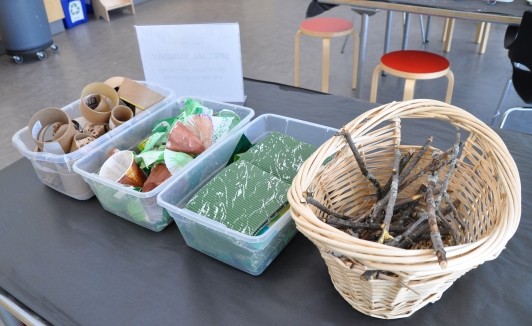 Bins set up with supplies: cardboard materials, painted found materials, collage papers, and sticks